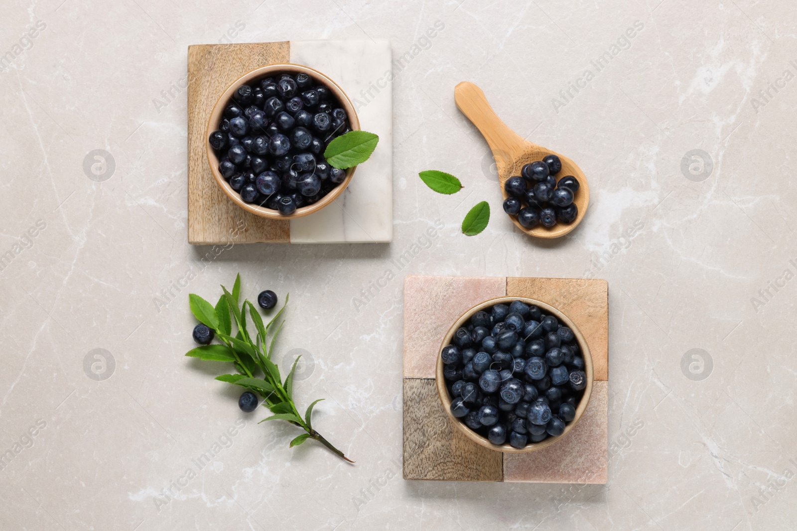 Photo of Tasty fresh bilberries and green leaves on light grey marble table, flat lay