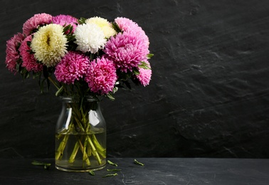 Beautiful asters in vase on table against black background, space for text. Autumn flowers