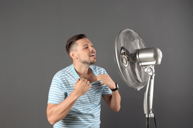 Man refreshing from heat in front of fan on grey background