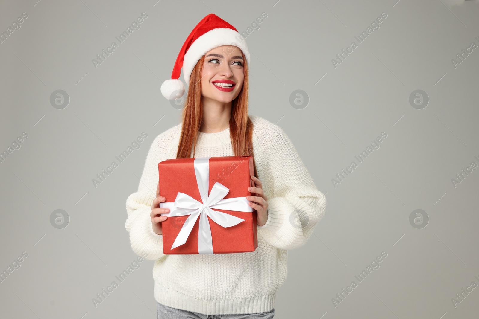 Photo of Young woman in Santa hat with Christmas gift on light grey background