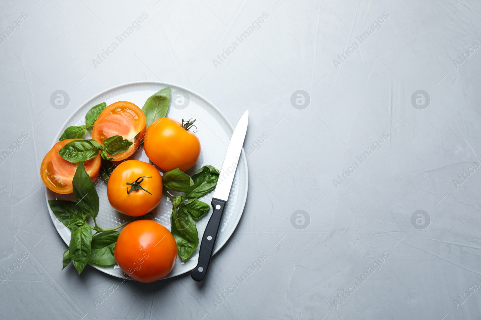 Photo of Ripe yellow tomatoes with basil on light grey table, top view. Space for text