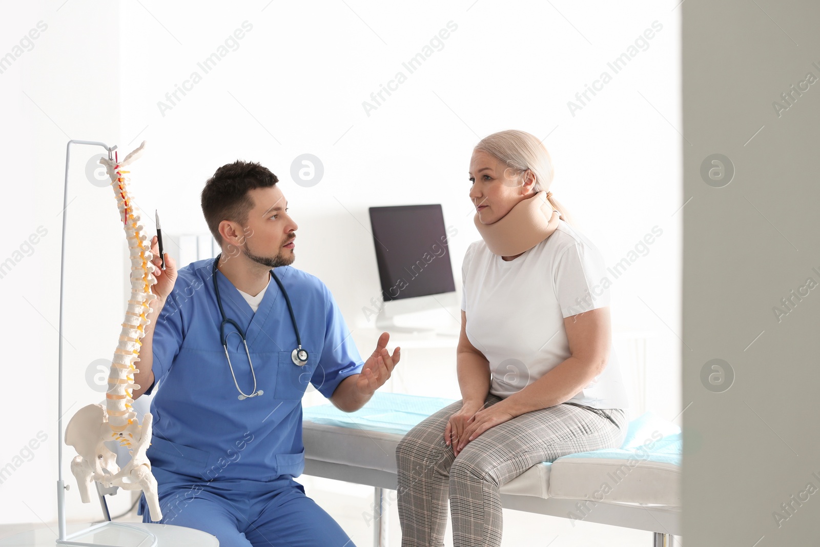 Photo of Male orthopedist explaining structure of spine to patient in clinic