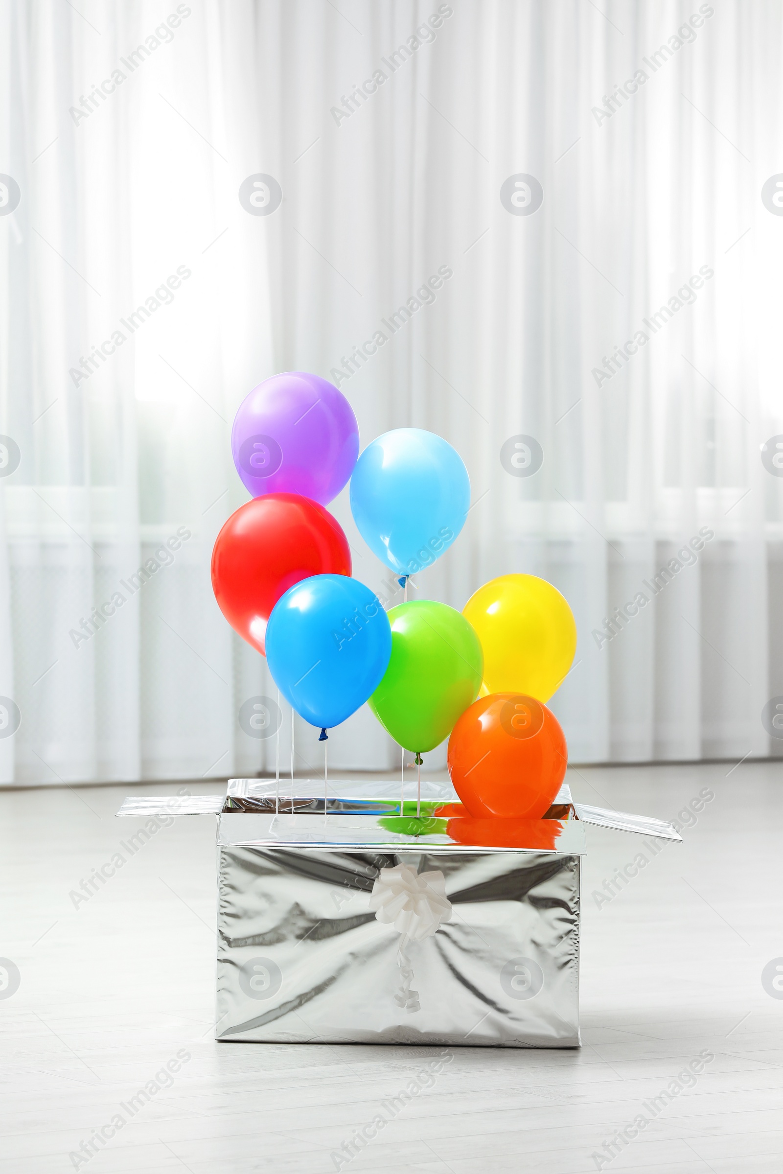 Photo of Gift box with bright air balloons on floor indoors