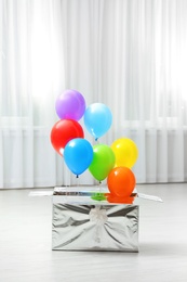 Gift box with bright air balloons on floor indoors