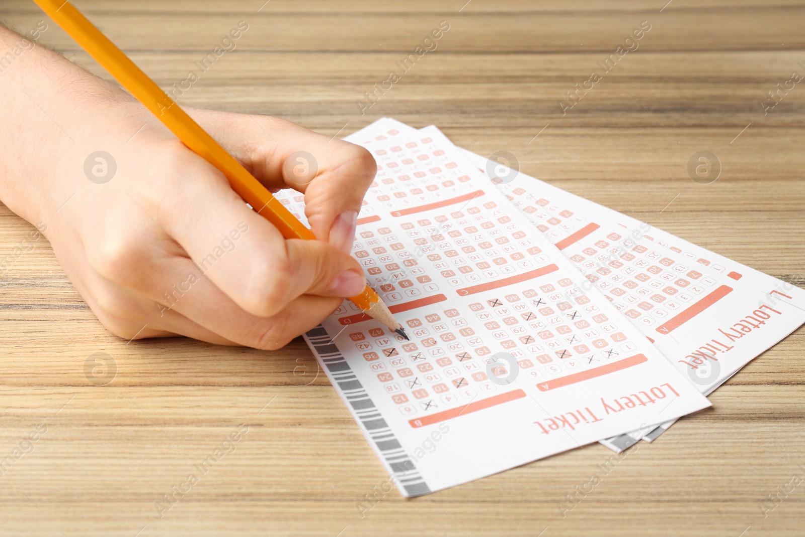 Photo of Woman filling out lottery tickets with pencil on wooden table, closeup. Space for text