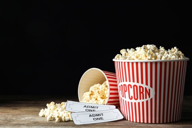 Popcorn and cinema tickets on wooden table against black background