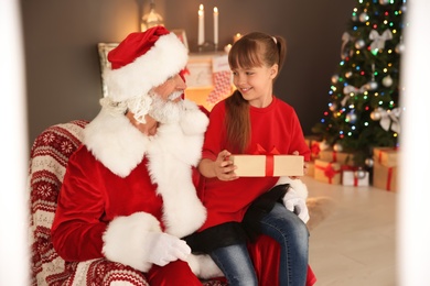 Little child with Santa Claus and Christmas gift at home, view through window