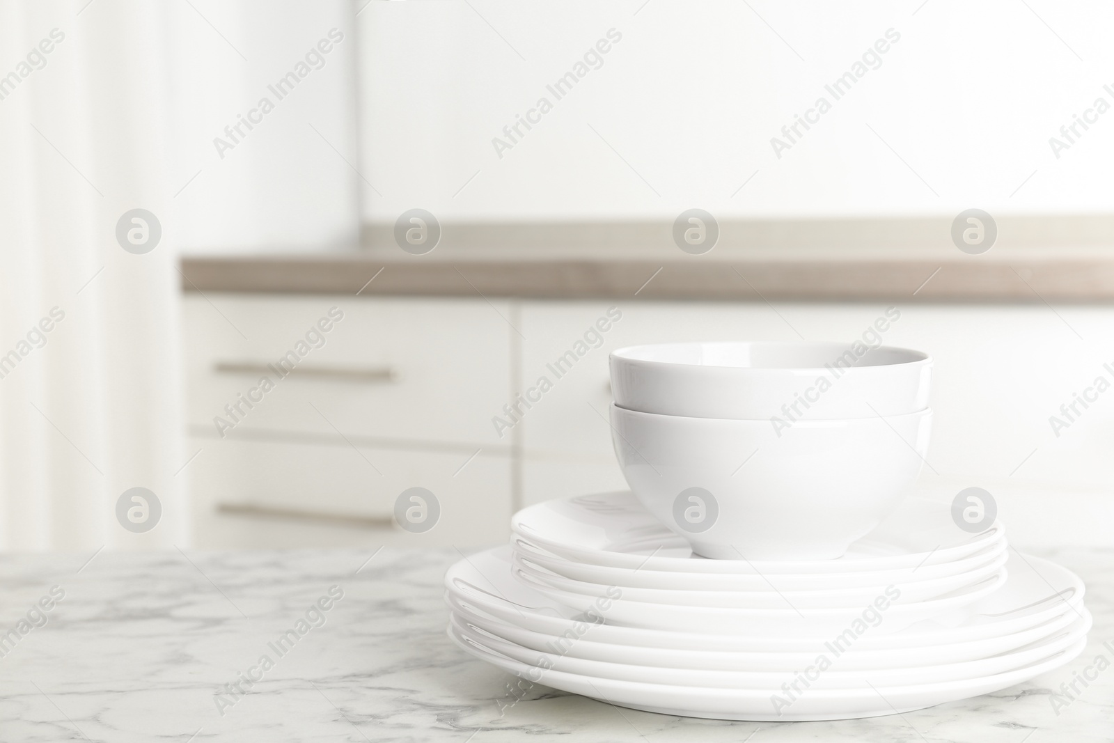 Photo of Stack of clean plates and bowls on marble table in kitchen. Space for text