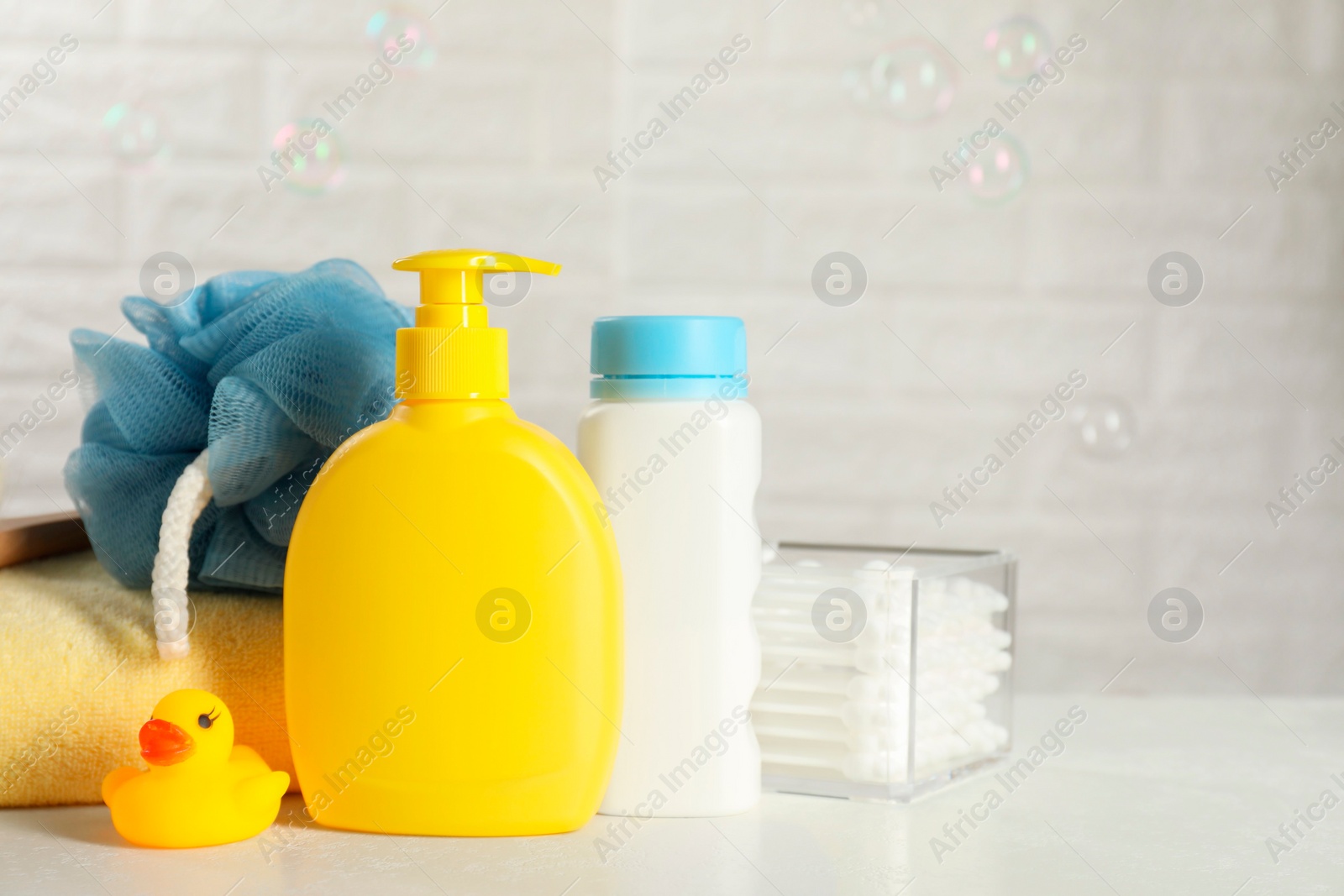 Photo of Baby cosmetic products, bath duck, cotton swabs and towel on white table against soap bubbles. Space for text