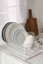 Drainer with different clean dishware and cup on light table indoors