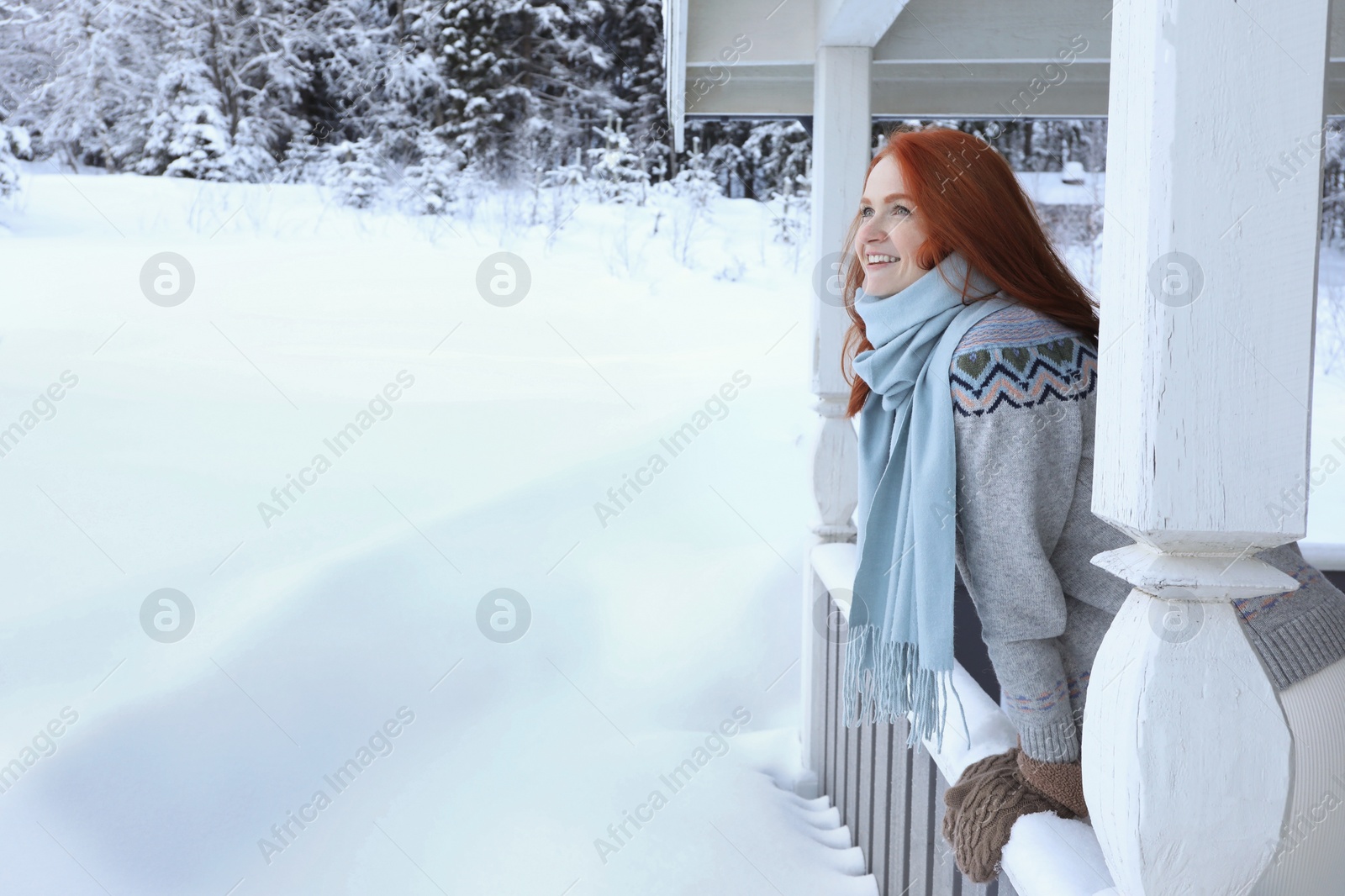 Photo of Beautiful young woman looking out from wooden gazebo on snowy day outdoors, space for text. Winter vacation