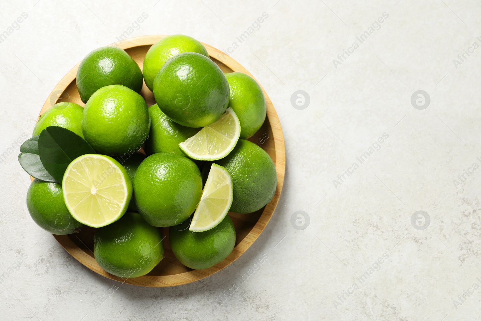Photo of Fresh ripe limes and green leaves on light table, top view. Space for text