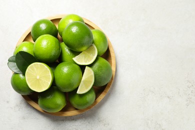 Photo of Fresh ripe limes and green leaves on light table, top view. Space for text