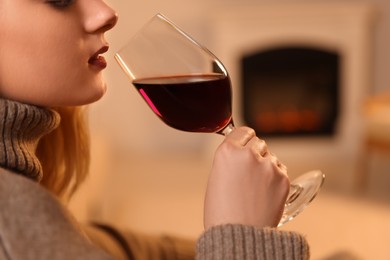 Photo of Young woman with glass of wine resting near fireplace indoors, closeup