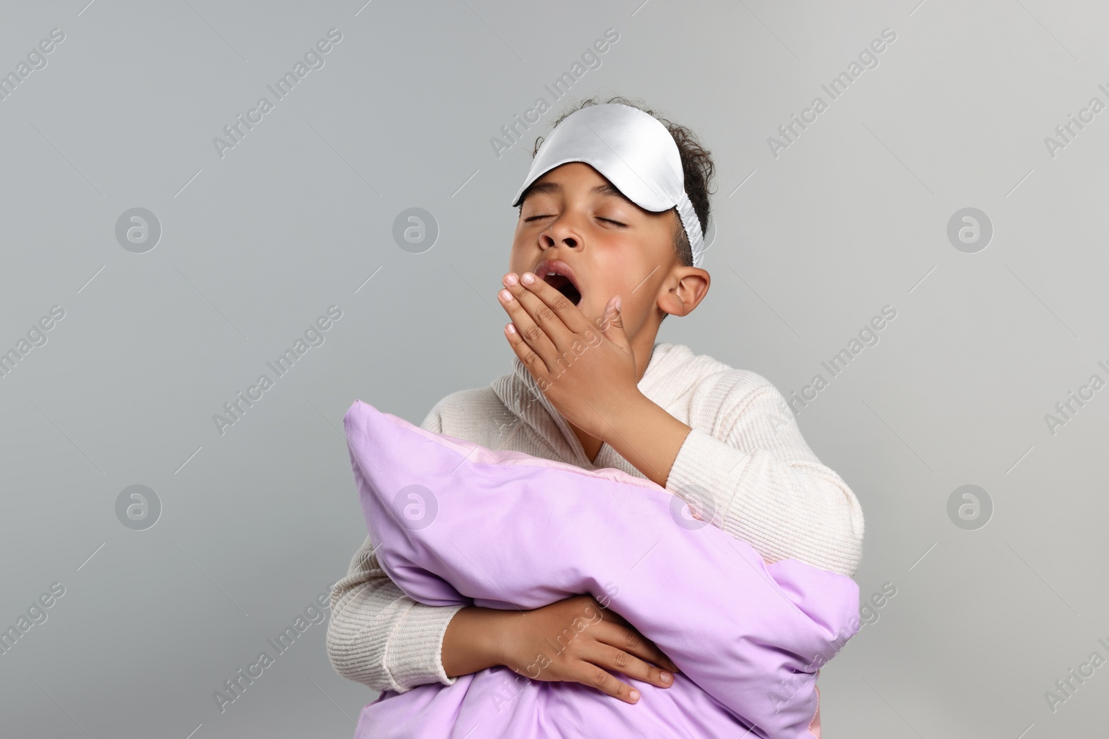 Photo of Boy with pillow and sleep mask yawning on grey background. Insomnia problem