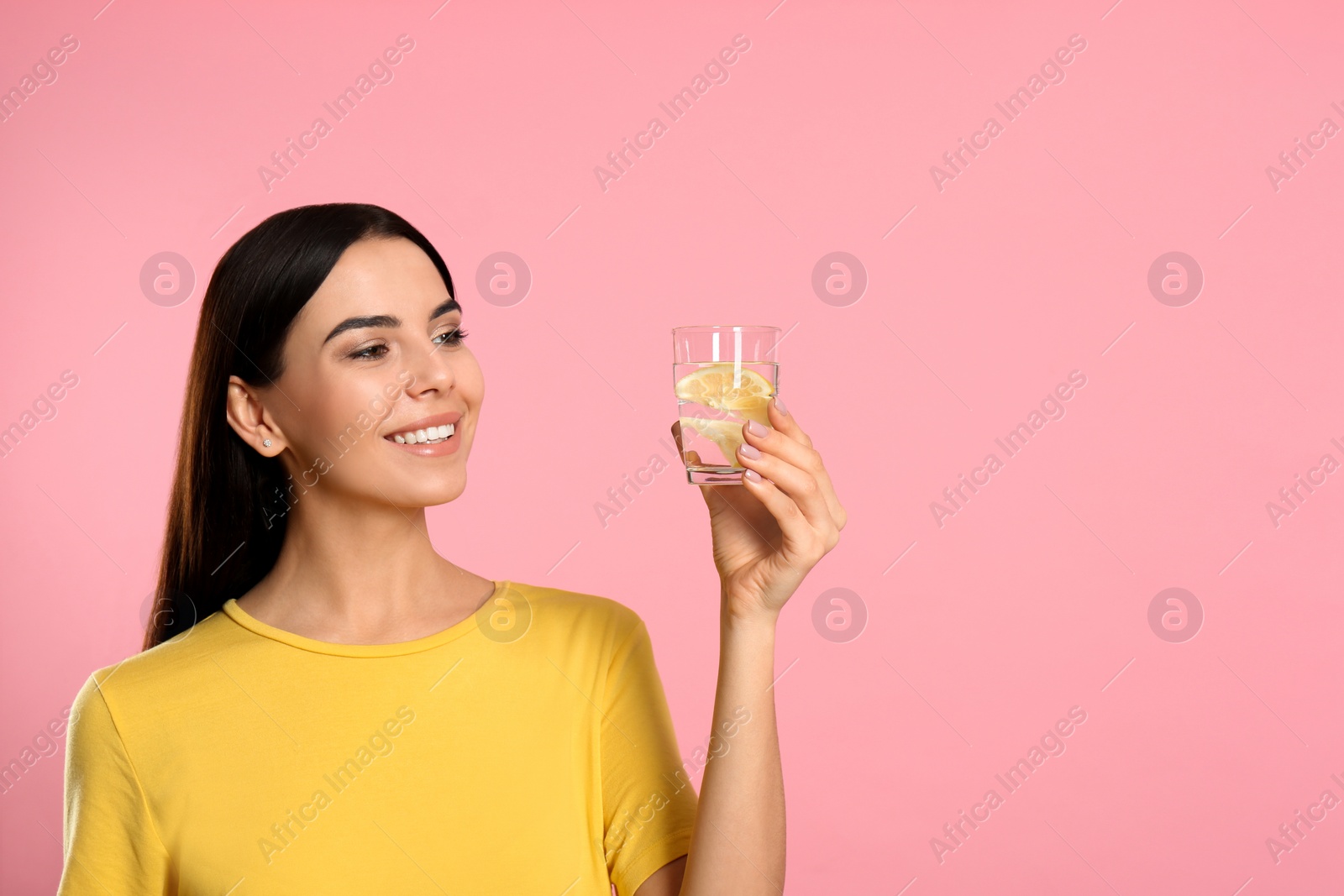 Photo of Beautiful young woman with tasty lemon water on pink background