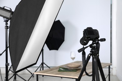 Photo of Table with stylish dinnerware in front of camera and professional lighting equipment indoors. Photo studio set