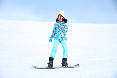 Photo of Young woman snowboarding on hill at mountain resort. Winter vacation