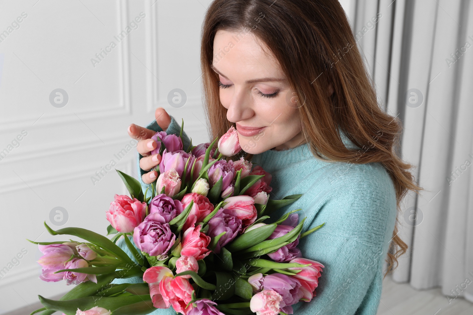 Photo of Young woman with bouquet of beautiful tulips indoors