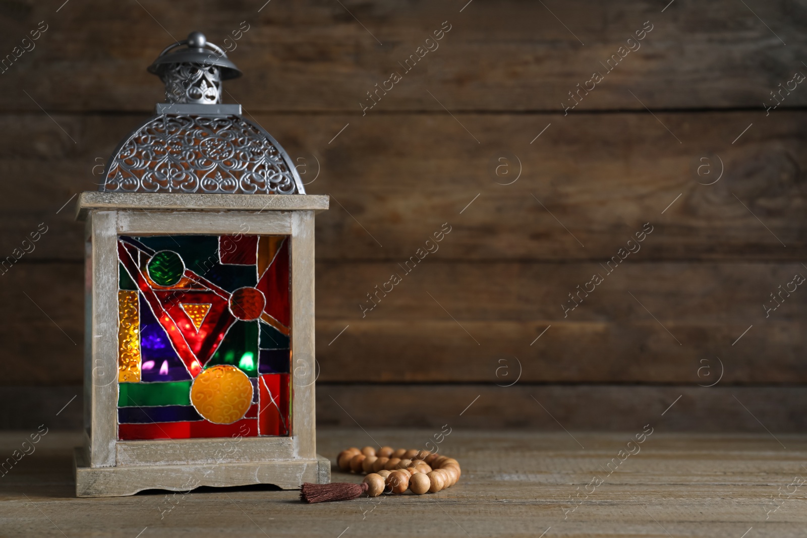 Photo of Decorative Arabic lantern and prayer beads on wooden table. Space for text