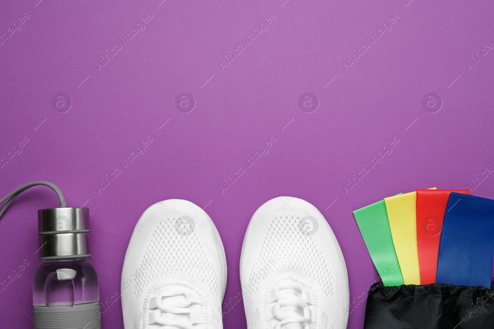 Photo of Set of fitness elastic bands, sneakers and bottle on purple background, flat lay. Space for text