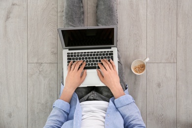 Photo of Young man using laptop while sitting on floor, top view