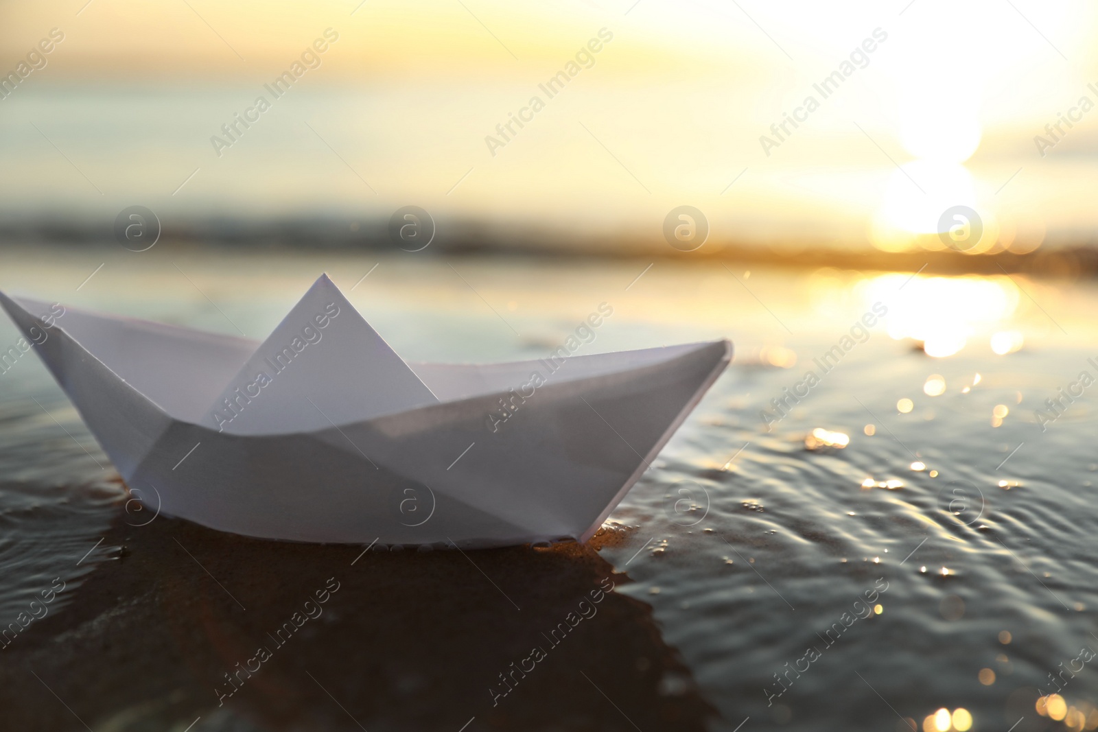 Photo of White paper boat in shallow water of sea at sunset, space for text