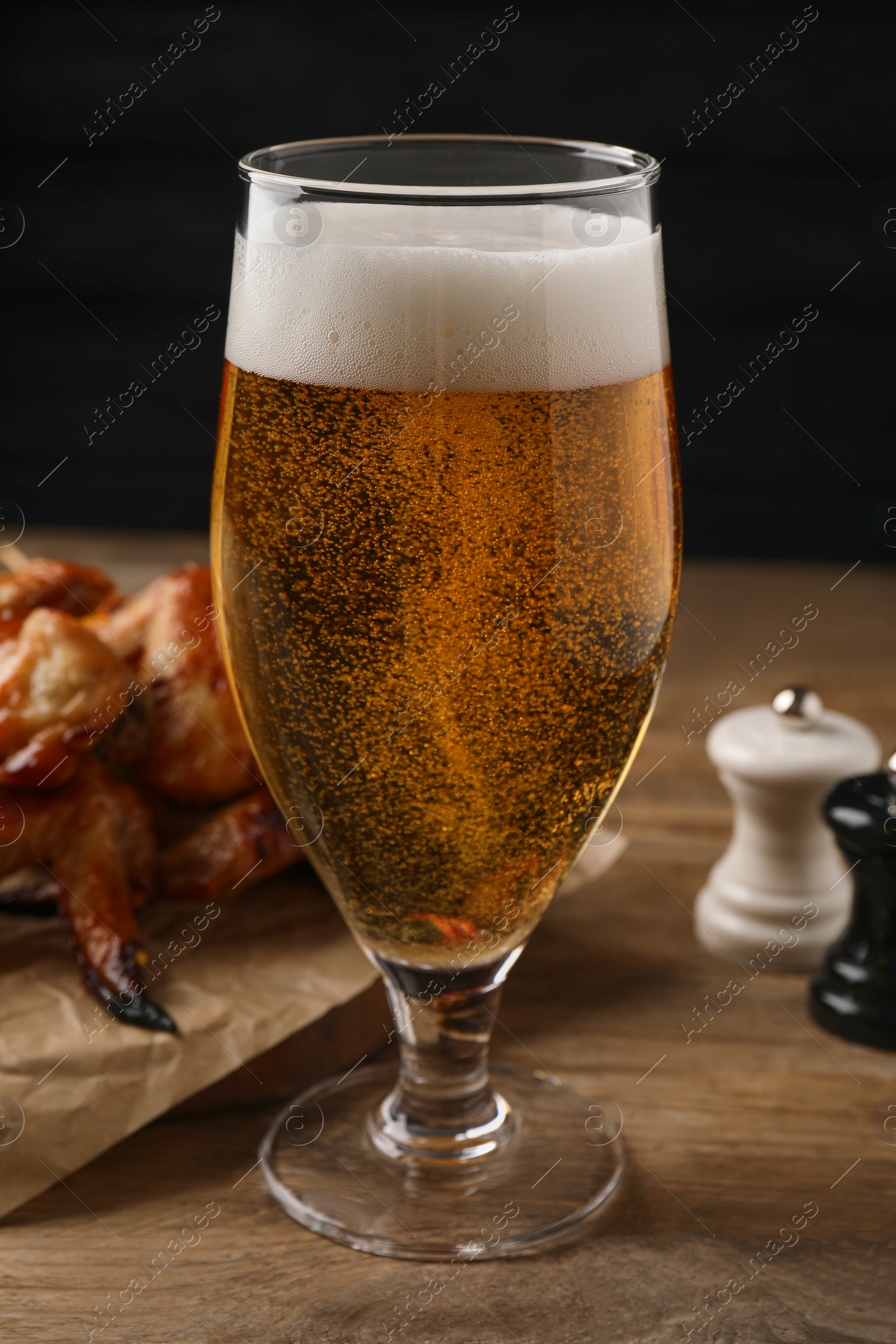 Photo of Glass of beer, delicious baked chicken wings and sauce on wooden table against black background