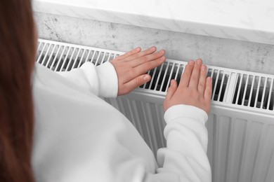 Girl warming hands on heating radiator indoors, closeup