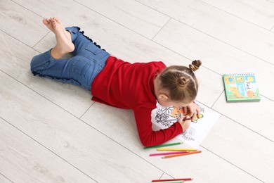 Photo of Cute little girl coloring on warm floor indoors. Heating system