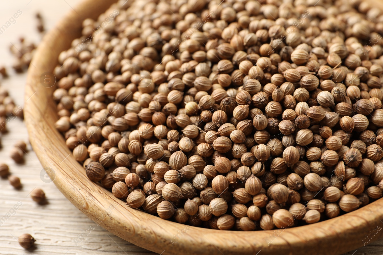 Photo of Dried coriander seeds in bowl on wooden table, closeup