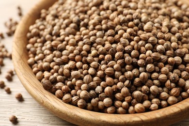 Photo of Dried coriander seeds in bowl on wooden table, closeup