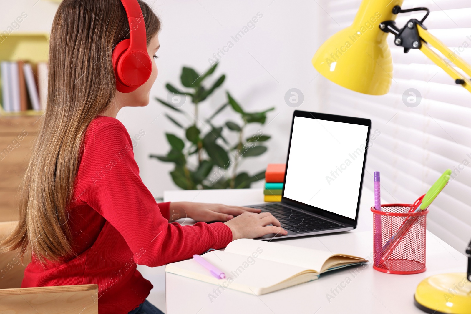 Photo of E-learning. Girl using laptop and headphones during online lesson at table indoors