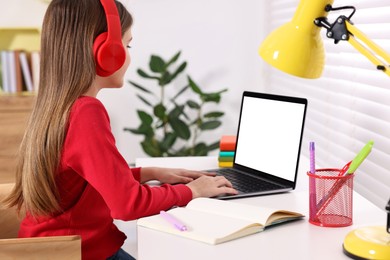 E-learning. Girl using laptop and headphones during online lesson at table indoors