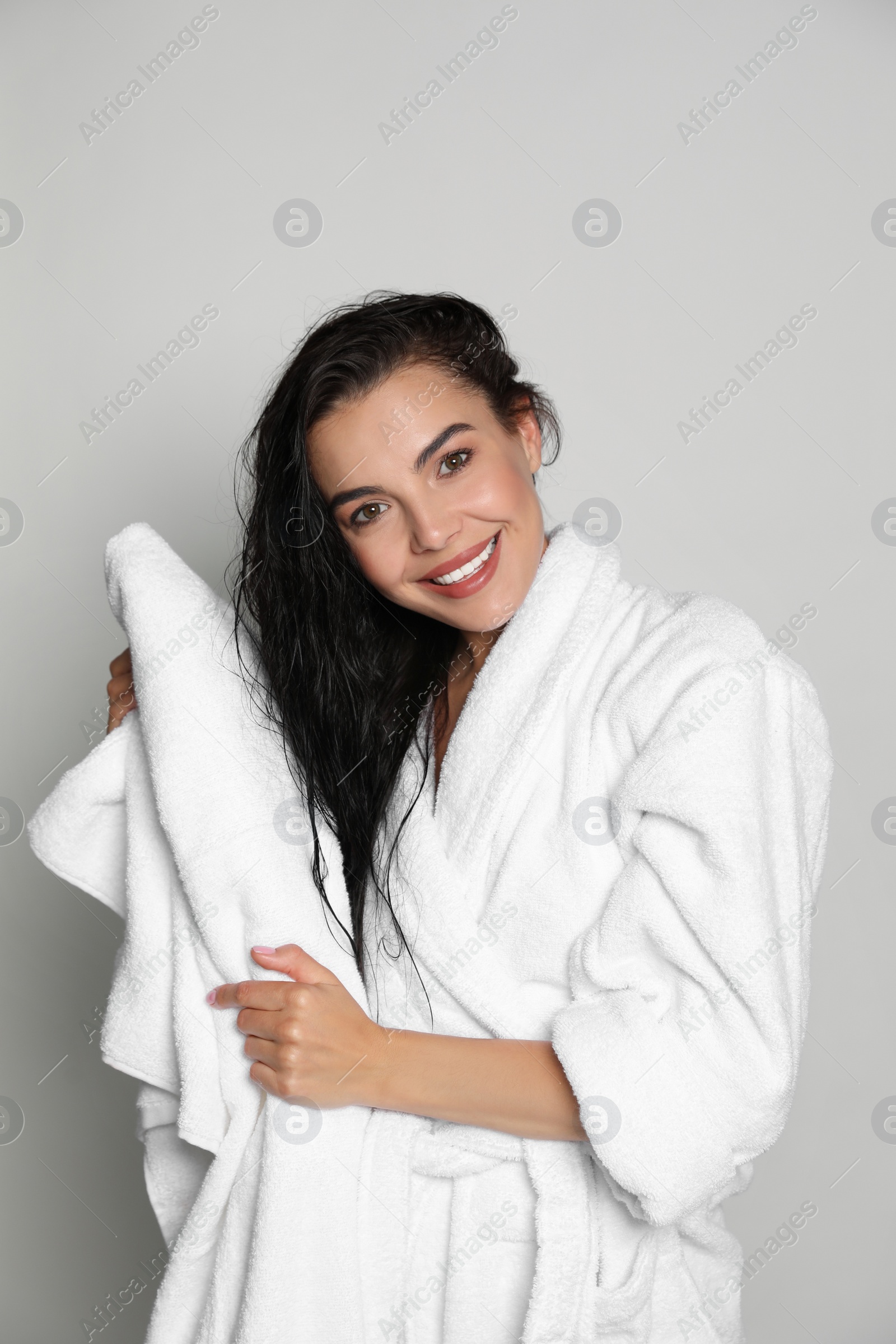 Photo of Beautiful young woman in bathrobe drying hair with towel on light background