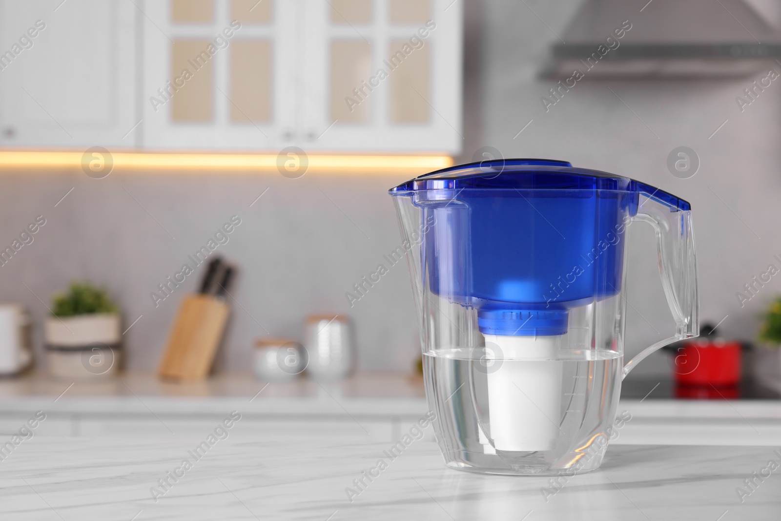 Photo of Water filter jug on white marble table in kitchen, closeup. Space for text