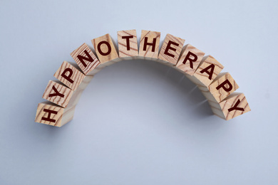 Photo of Wooden blocks with word HYPNOTHERAPY on light background, flat lay