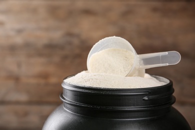 Photo of Black jar with measuring scoop of protein powder against wooden background, closeup