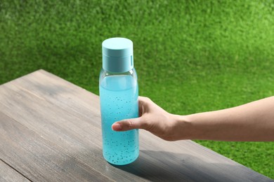 Photo of Woman holding bottle of light blue drink at wooden table outdoors, closeup