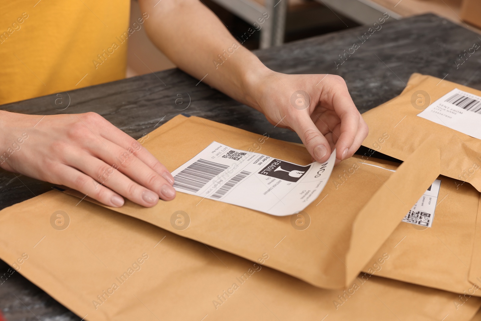 Photo of Post office worker sticking barcode on parcel at counter indoors, closeup