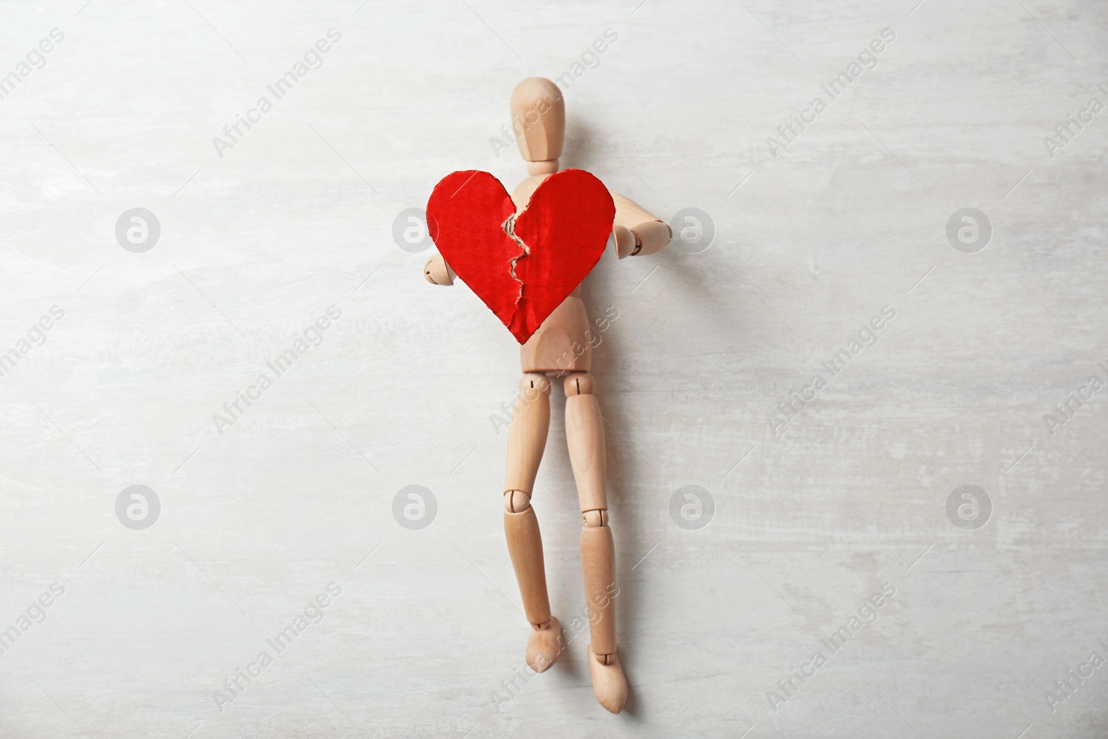 Photo of Wooden puppet with torn cardboard heart on gray background. Relationship problems