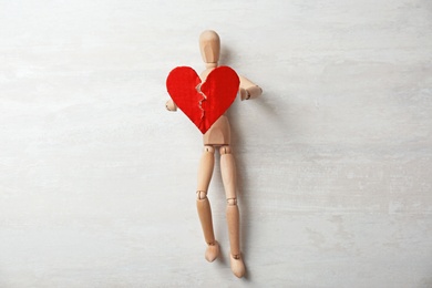 Wooden puppet with torn cardboard heart on gray background. Relationship problems