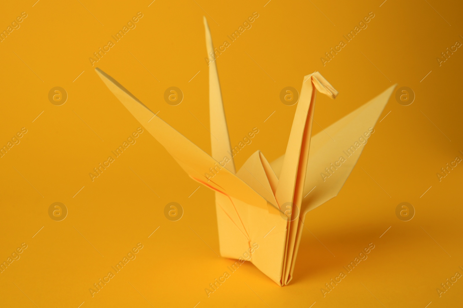 Photo of Origami art. Beautiful light yellow paper crane on orange background