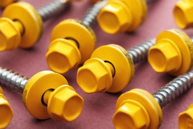 Yellow self-tapping screws on pink background, closeup