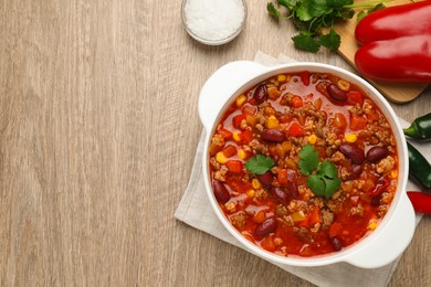 Photo of Bowl with tasty chili con carne and different ingredients on wooden table, flat lay. Space for text