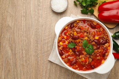 Bowl with tasty chili con carne and different ingredients on wooden table, flat lay. Space for text