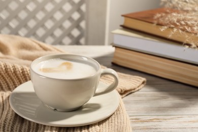 Cup of tasty coffee near sweater and stack of books on white wooden table