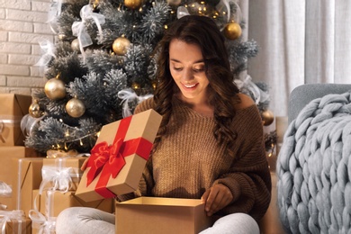 Image of Happy young woman opening Christmas gift at home. Magic holiday 