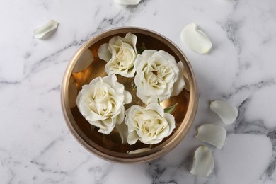 Photo of Tibetan singing bowl with water and beautiful roses on white marble table, top view