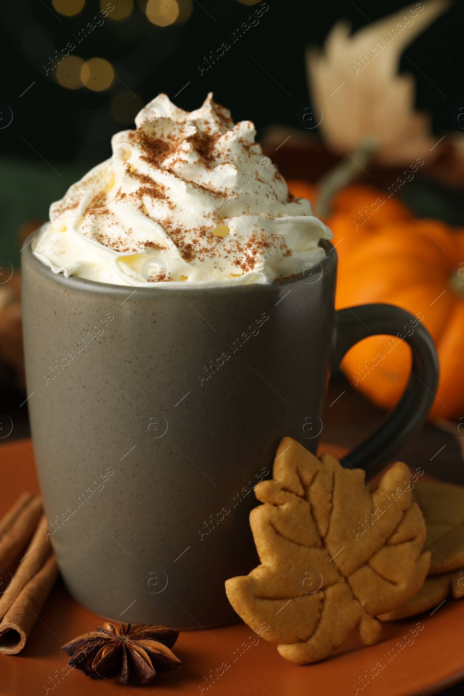 Photo of Tasty pumpkin spice latte with whipped cream in cup and cookies on table, closeup